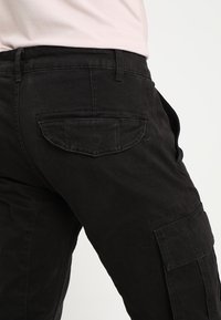 Czarne spodnie cargo z przednimi i tylnymi kieszeniami, o lekko luźnym kroju oraz solidnym materiale o gładkiej fakturze.