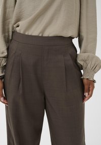 Pruunid volditud laiad püksid sileda tekstuuriga, millel on kõrge vöökoht. Koos heleda beeži bluusiga, millel on volüümsed varrukad.