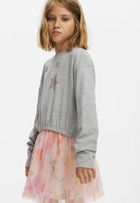 Szürke, rövidített pulóver csillag díszítéssel, amelyet pasztell tüll szoknyával párosítottak, amelyen csillag motívumok és rétegezett kialakítás található.