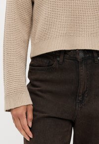 Beige gebreide trui met een textuurpatroon, voorzien van geribbelde manchetten. Combinatie met donkerbruine spijkerbroek, die een klassieke pasvorm en zakken heeft.