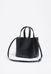 Zwarte leren tote bag met dubbele handvaten aan de bovenkant en een lange verstelbare schouderband. Gladde textuur, open ontwerp met minimale stiksels en zonder hardware.