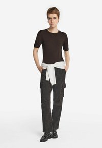 Brun strikket t-shirt med korte ærmer, parret med mørke cargo bukser og en hvid sweater bundet om taljen. Sorte loafers fuldender looket.