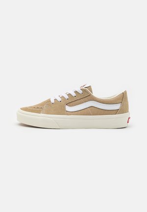 Zapatilla de ante marrón con costuras y cordones blancos, que presenta una franja lateral blanca y una suela de goma crema en contraste. Diseño simple y clásico.
