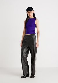 Haut sans manches violet, pantalon en simili cuir noir avec des rayures latérales blanches, casquette noire, porté avec des bottines noires. Coupe droite et design ajusté.