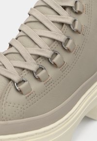 Beige Leder-Sneaker mit strukturierter Oberfläche, flachen beigen Schnürsenkeln, silbernen Beschlägen und einer hellen Gummisohle mit Nähdetails.