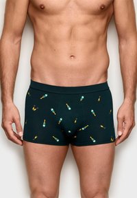 Dunkelgrüne Boxershorts aus weichem Stoff mit einem wiederholten Muster von Champagnerflaschen und Gläsern in Gelb und Türkis.