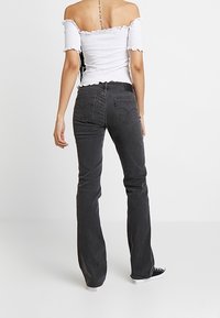 Jean évasé noir à taille haute, avec poches arrière et une légère élasticité. Associé à un haut blanc épaules dénudées. Apparence texturée.