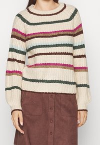 Stickad tröja med krämfärgad bas och flerfärgade ränder i rosa, grönt, brunt och blått. Har en ribbad rundhalsning och muddar.