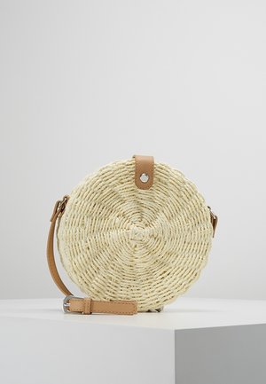 Borsa rotonda in paglia intrecciata color crema, con una tracolla in pelle marrone e design circolare con superficie testurizzata. Dettaglio in metallo nella parte superiore.