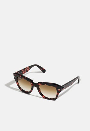 Occhiali da sole con tonalità marroni e montatura marmorizzata nera e rossa. Design squadrato con aste spesse, con dettagli del logo sul lato.