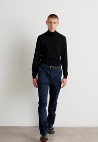 Czarny sweter z golfem, granatowe spodnie cargo z kieszeniami i czarne buty z czerwonymi akcentami. Prosty design, dopasowany krój, gładka tekstura.