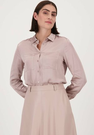 Licht mauve zijden overhemd met knopen, voorzien van twee borstzakken, lange mouwen en een kraag. Draagt bij een bijpassende hoge taille rok.