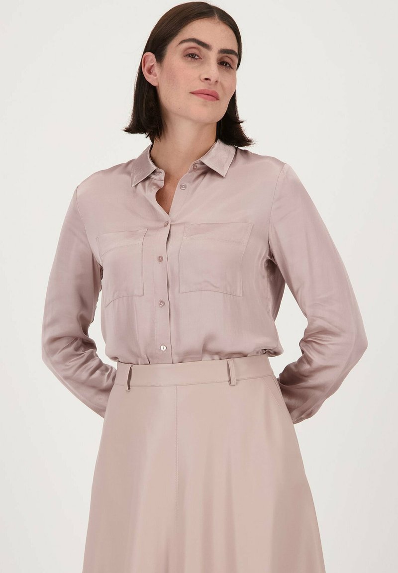 Licht mauve zijden overhemd met knopen, voorzien van twee borstzakken, lange mouwen en een kraag. Draagt bij een bijpassende hoge taille rok.