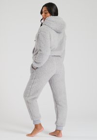 Grauer, flauschiger Fleecejumpsuit mit Kapuze, elastischen Bündchen und Seitentaschen. Weicher Stoff, lockere Passform und mittelhohes Design.