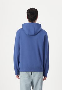 Blå hettegenser med avslappet passform, ribbede mansjetter og hem, myk tekstur og et enkelt design, brukt sammen med lyseblå jeans.