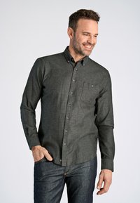 Camisa de manga larga gris oscuro con collar abotonado, bolsillo frontal y botones en contraste, combinada con jeans de mezclilla oscuros. Textura de tela suave.