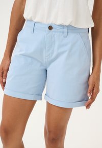 Ljusblå bomullsshorts med figursydd midja, uppvikta fållar, sidofickor och en dekorativ brun knapp framtill. Slät textur.