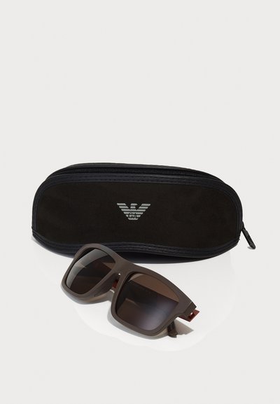 Ochelari de soare supradimensionați, maro, cu lentile închise la culoare și un finisaj mat, însoțiți de un toc negru cu fermoar, decorat cu un logo minimalist.