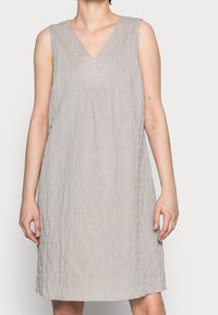Jasnoszara, bezrękawnikowa sukienka z dekoltem w kształcie litery V, o teksturowanej tkaninie, z marszczeniami z przodu oraz luźnym krojem w kształcie litery A.