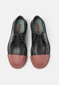Bottines en cuir noir avec un capuchon en caoutchouc brun brillant, design à lacets et semelle intèrieure colorée avec des flecks, arborant le logo "Camper".