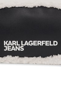 Saco de couro preto com acabamento felpudo branco, apresentando "KARL LAGERFELD JEANS" em letras brancas, negrito e arredondadas. Superfície texturizada com elementos suaves e lisos.