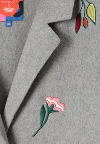 Blazer in misto lana grigio con ricami floreali rosa e verdi sulla pattina sinistra, dotato di colletto rigido e vestibilità sartoriale.