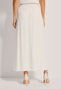 Weißer Maxirock mit einem elastischen Bund, fließendem Stoff und minimaler Textur, kombiniert mit beigen High-Heels.
