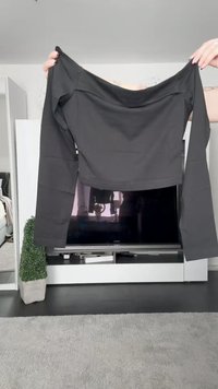 Must_have musta pikkade varrukatega crop-top, mis on valmistatud siledast kangast, laia kaelusega ja istuvate varrukatega. Taustal on televiisor ja toataimed.