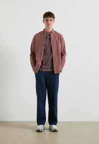 Licht bordeaux kleurig overhemd met knopen, marineblauwe broek en grijze sneakers. Het overhemd heeft een zachte textuur en contrasterende strepen eronder.