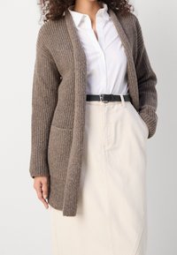 Ribbad långärmad cardigan i taupe ullblandning, med öppen framsida och två framfickor, bärs över en vit skjorta och krämfärgad kjol.