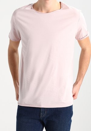 Lichtroze t-shirt met korte mouwen van zachte stof, met een ronde halslijn en een relaxte pasvorm, gecombineerd met donkerblauwe spijkerbroek.