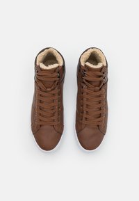 Brown leather high-top sneakers with a fluffy tan lining, black eyelets, and matching brown laces. White rubber sole.