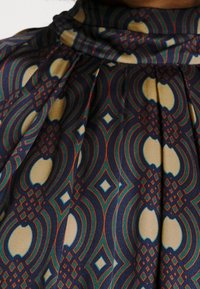 Kuosisella kankaalla, jossa on sinisiä, kermaisia ja ruosteenvärisiä sävyjä; siinä on geometrisia kuvioita, kuten timantteja ja kaarevia muotoja, pehmeiden laskosten kera.