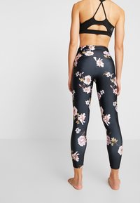Zwarte sportbeha met een racerback ontwerp, gecombineerd met strakke leggings met een bloemenpatroon op een donkere achtergrond.