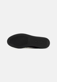 Semelle de chaussure en caoutchouc noir avec texture rainurée et canaux de drainage verticaux pour une meilleure adhérence. Forme courbée avec un logo visible.