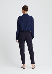 Marineblauw overhemd met lange mouwen gecombineerd met op maat gemaakte marineblauwe broek. Het overhemd heeft een kraag en een rugpand; de broek heeft een taps toelopende pijp en een manchet aan de onderkant.