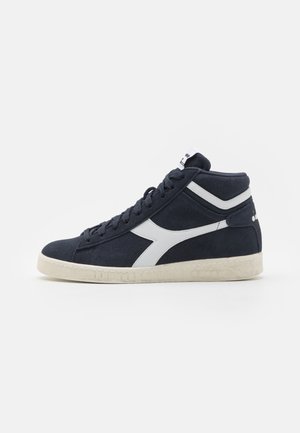 High-top athletic shoes in navy suede with white accents, featuring laces, a textured sole, and a logo near the ankle.