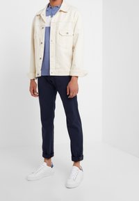 Světlý béžový denimový sak přes modro-bíle pruhovaný polo, v kombinaci s námořnickými kalhotami a bílými teniskami s modrými akcenty.