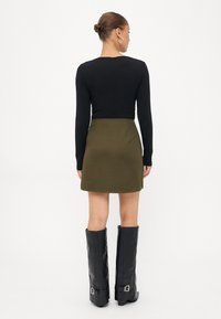 Zwarte lange mouwen top in combinatie met een olijfgroene minirok. Zwarte kniehoog laarzen met een gespsluiting. Soepele stoftextuur.