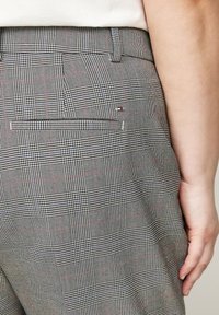 Šedé kostkované kalhoty s texturovanou tkaninou, zadní kapsou a jemnými červenými a modrými akcenty v vzoru. Poutka na pásek v pase.