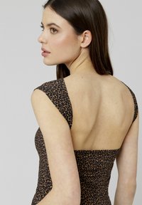 Robe ajustée en imprimé léopard avec de larges bretelles, dos carré et texture lisse. Motif marron et noir, affichant un design minimaliste.