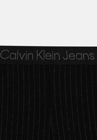 Tissu noir côtelé avec de fines rayures verticales, doté d'une large ceinture portant en relief "Calvin Klein Jeans" en gris.