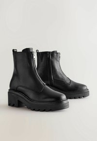 Black leather ankle boots with a textured finish, side zippers, and chunky rubber soles featuring a jagged tread pattern.
