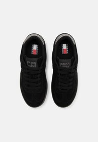 Paire de baskets Tommy Jeans noires avec lacets, logo visible sur la languette et la semelle intérieure, vue de dessus sur fond blanc.