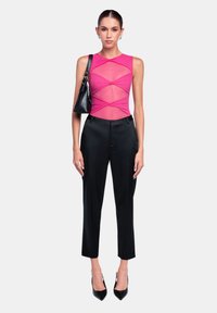 Top in rete rosa aderente con design incrociato, abbinato a pantaloni neri su misura e tacchi a punta neri. Borsa nera con tracolla.