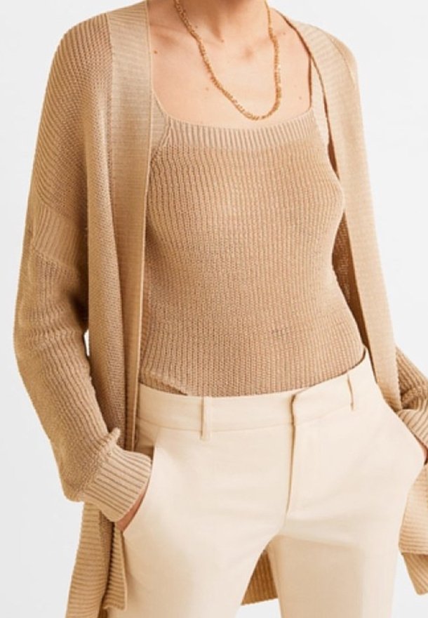 Beige knitted cardigan over a matching ribbed tank top, paired with light beige tailored pants. Features textured fabrics and a relaxed fit.