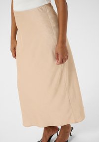 Jupe beige longue en A, en tissu doux avec une texture subtile. Dotée d'une taille lisse, elle tombe jusqu'aux chevilles.