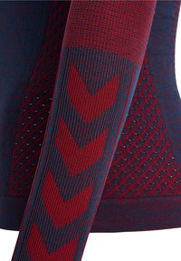 Lähellä oleva kuva punaisesta ja tummansinisestä neulotusta kankaasta, jossa on chevron-kuvioita hihassa ja teksturoituja viistoperforointiyksityiskohtia vartalossa.