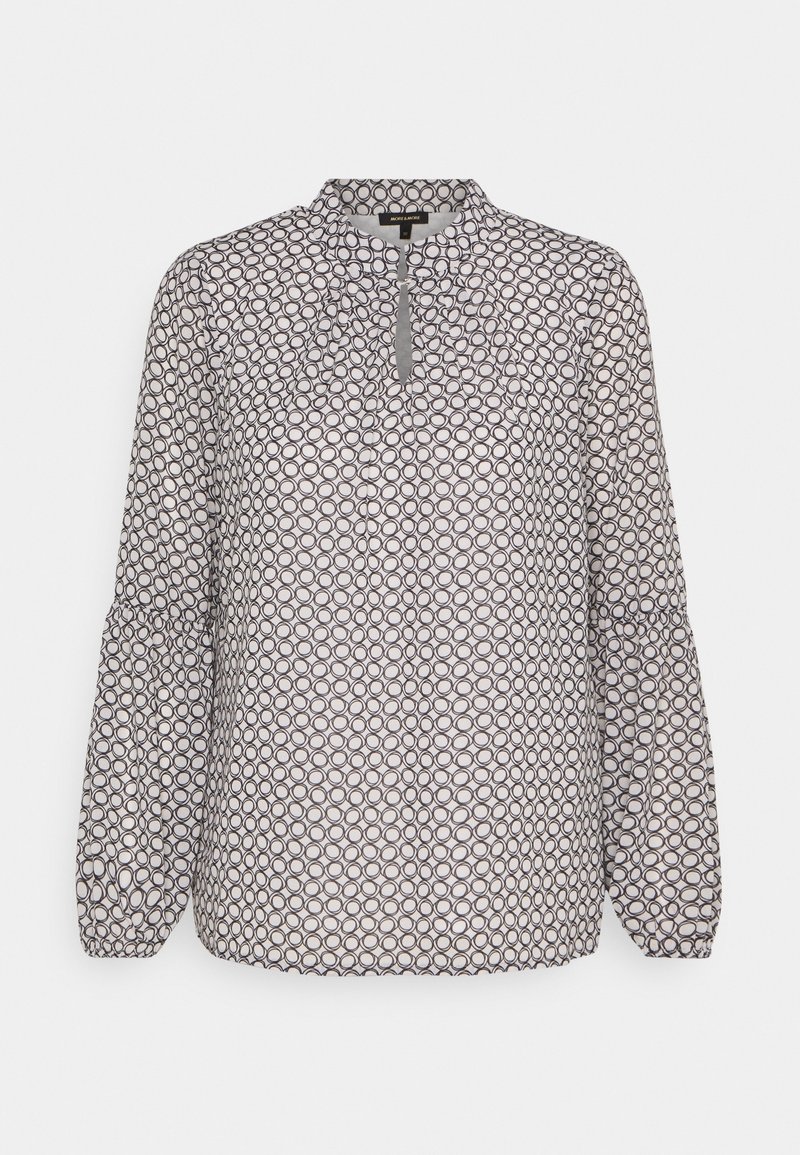 Blouse à manches longues avec col montant et motif de cercles noir et blanc, avec poignets froncés et ouverture en forme de goutte à l'avant.