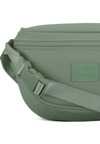 Green fabric crossbody bag with a smooth texture, zipper closure, adjustable strap, and a rectangular logo patch on the side.